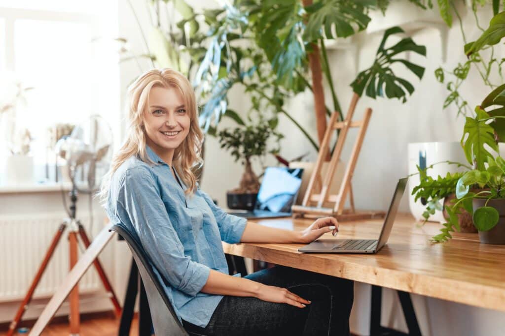 Joyful female business person works on her laptop in office with plants